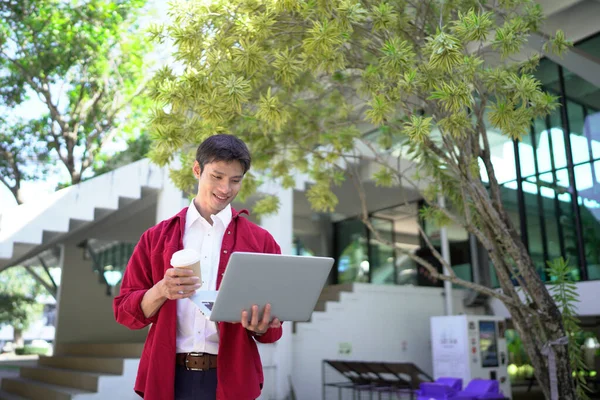 Uzaktan çalışan, kahve içen ve şehir parkında dizüstü bilgisayar kullanan bir adam..