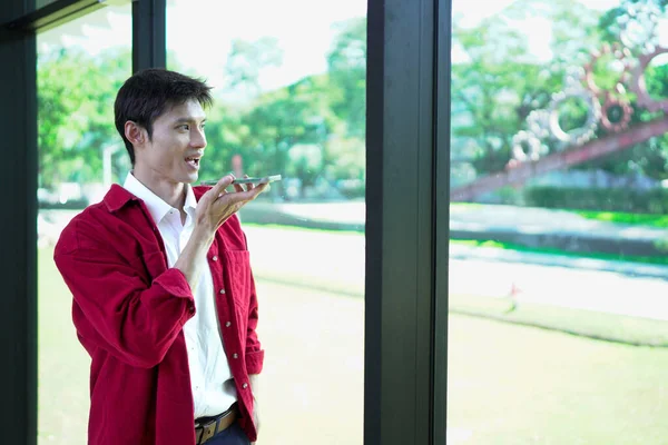 Genç bir adam sesli komut kullanıyor ya da akıllı telefonuyla yapay zeka asistanı ile iletişim kuruyor..