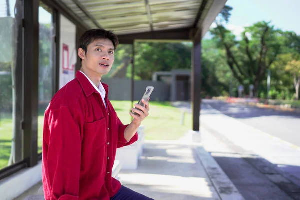 Akıllı telefonlu genç adam otobüs durağında toplu taşıma bekliyor..