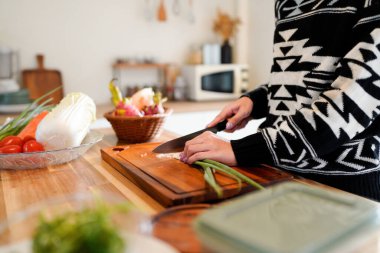 Mutfakta ahşap bir kesme tahtasının üzerinde yeşil soğan doğrayan bir insan...