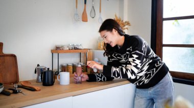 Bir kadın kahve öğütücüsünde kahve çekirdeklerini öğütüyor. Kahve öğütücüsü diğer birkaç eşyanın yanında, ahşap bir masanın üzerinde..