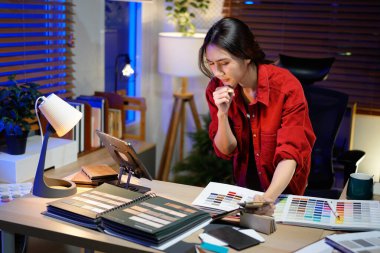 Gece Modern Ofis Alanında Dizüstü bilgisayar kullanarak Ev Tasarımı Projesi için Renk Paleti ve Malzeme Örnekleri Seçen Asyalı İç Tasarımcı.