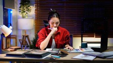 Gece Modern Ofis Alanında Dizüstü bilgisayar kullanarak Ev Tasarımı Projesi için Renk Paleti ve Malzeme Örnekleri Seçen Asyalı İç Tasarımcı.