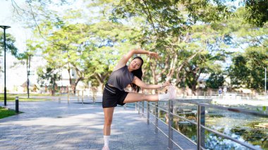 Sağlıklı genç Asyalı koşucu kadın sıcak bir ışık altında parkta egzersiz yapmadan önce vücudu ısıtıyor. Yaşam tarzı fitness ve aktif kadınlar şehir konseptinde egzersiz yapıyorlar..