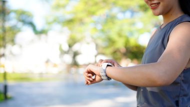 Aktif gülümseyen genç bir kadının yaz aylarında parkta yapılacak sağlık egzersizi sırasında spor yapma durumunu kontrol etmesi..