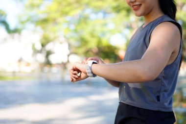 Gülümseyen sporcu kadın parkta spor yaptıktan sonra akıllı bakışlarını kontrol ediyor..