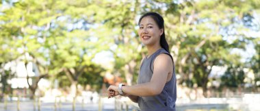 Genç bir kadın dışarıda egzersiz yaparken akıllı saati kontrol ediyor. Fitness izleme, egzersiz rutini, sağlık izleme ve giyilebilir teknolojiyle aktif yaşam tarzı kavramı..