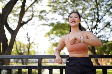 Genç bir kadın dışarıda egzersiz yaparken akıllı saati kontrol ediyor. Fitness izleme, egzersiz rutini, sağlık izleme ve giyilebilir teknolojiyle aktif yaşam tarzı kavramı..