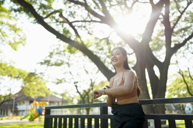 Genç bir kadın dışarıda egzersiz yaparken akıllı saati kontrol ediyor. Fitness izleme, egzersiz rutini, sağlık izleme ve giyilebilir teknolojiyle aktif yaşam tarzı kavramı..