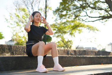 Kadın, kulaklık ve müzik parkta egzersiz için mola veriyor ve bir ağacın yanında dinleniyor. Egzersiz.