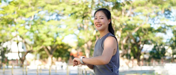 Genç bir kadın dışarıda egzersiz yaparken akıllı saati kontrol ediyor. Fitness izleme, egzersiz rutini, sağlık izleme ve giyilebilir teknolojiyle aktif yaşam tarzı kavramı..