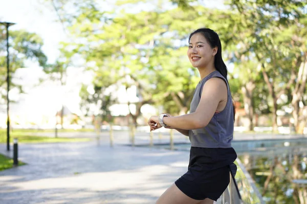 Genç bir kadın dışarıda egzersiz yaparken akıllı saati kontrol ediyor. Fitness izleme, egzersiz rutini, sağlık izleme ve giyilebilir teknolojiyle aktif yaşam tarzı kavramı..