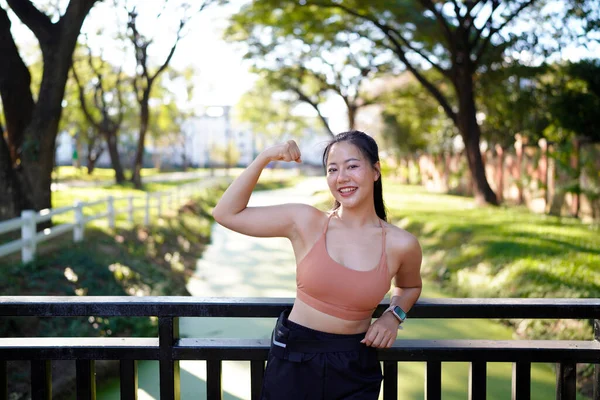 Kadın sporcu parkta kaslarını esnetiyor, dışarıdaki kameraya bakıyor..