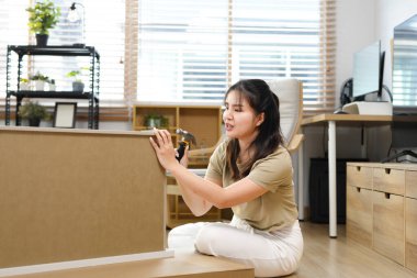 Çekiçli genç bir Asyalı kadın yeni bir eve taşındıktan sonra mobilya monte ediyor...