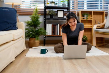 Rahatlamış bir kadın kahve içiyor ve evde otururken dizüstü bilgisayar kullanıyor..