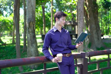 Elinde kahve fincanı olan bir adam ya da bahçede duran yeşil doğa arka planında duran tek kullanımlık kahve ve kitap. Mutlu insanları boş vakitlerinde kabul et ve kahve iç...