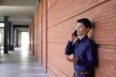 Gülümseyen iş adamı cep telefonuyla dışarıda oturuyor..