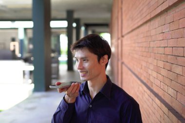 Gülümseyen iş adamı cep telefonuyla dışarıda oturuyor..