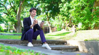 Gülümseyen işadamı akıllı telefon kullanıyor ve ofis binasının dışında kahve tutuyor..