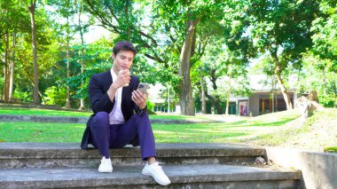 Gülümseyen işadamı akıllı telefon kullanıyor ve ofis binasının dışında kahve tutuyor..