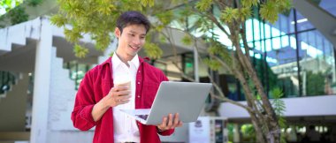 Uzaktan çalışan, kahve içen ve şehir parkında dizüstü bilgisayar kullanan bir adam..