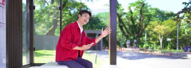 Akıllı telefonlu genç adam otobüs durağında toplu taşıma bekliyor..