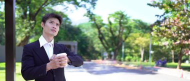 Siyah takım elbiseli bir işadamı kahve fincanı tutuyor, saatine bakıyor ve taksi bekliyor..