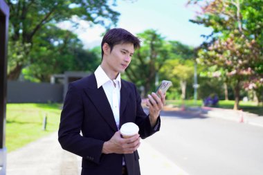 Asyalı işadamı otobüs durağında beklerken akıllı telefon kullanıyor.