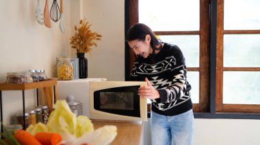 side view of smiling woman in shirt using microwave in kitchen.