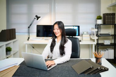 Modern ofisteki iş yerinde dizüstü bilgisayarla çalışan kendine güvenen bir iş kadını...