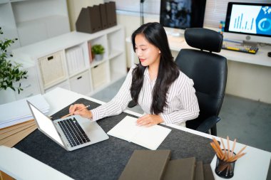 Modern ofisteki iş yerinde dizüstü bilgisayarla çalışan kendine güvenen bir iş kadını...