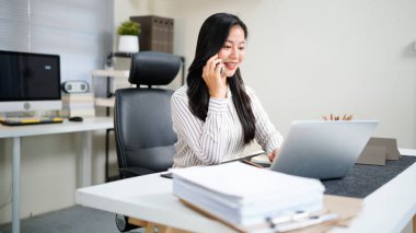 Genç Asyalı iş kadını. Güzel, çekici, gülümseyen ve ofisteki cep telefonuyla konuşan...