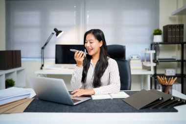 Voice note, chatting or talking of a woman on the phone at work in the office. Businesswoman talking on her speaker sending a voicemail or audio message to a colleague about work plan or schedule..