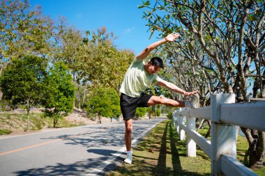 Parkta koşmadan önce esneyen bir adamın fotoğrafı, spor kıyafetleri, açık hava spor kıyafetleri ve doğal ortamdaki sağlık aktiviteleri..