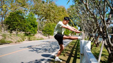 Parkta koşmadan önce esneyen bir adamın fotoğrafı, spor kıyafetleri, açık hava spor kıyafetleri ve doğal ortamdaki sağlık aktiviteleri..