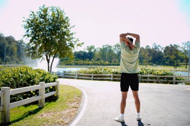 Parkta koşmadan önce esneyen bir adamın fotoğrafı, spor kıyafetleri, açık hava spor kıyafetleri ve doğal ortamdaki sağlık aktiviteleri..