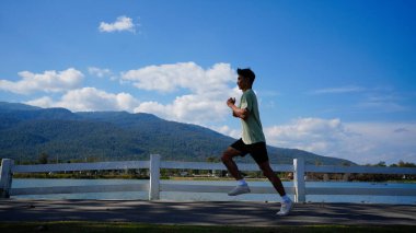 Yolda koşan genç bir adamın silueti. Açık havada peyzaj ve gökyüzü arkaplanlı spor yaparken formda bir fitness koşucusu.