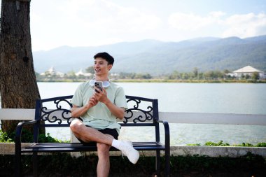 Kamu parkında cep telefonu tutan Asyalı bir adam, akıllı telefon kullanan bir erkek mobil fitness uygulaması kullanıyor.