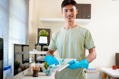 Person cleaning room, cleaning worker is using cloth to wipe computer keyboard in company office room. Cleaning staff. Concept of cleanliness in the organization.