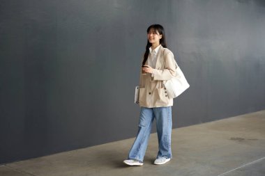 Güzel bir kadın kahve fincanıyla işe giderken ofis binasının yanında yürüyor. Başarılı bir iş, Asyalı kız elinde bir bardak sıcak içecek, laptopuyla işe giderken yolda..