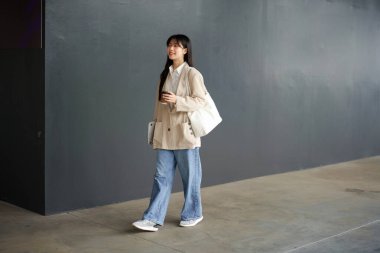 Güzel bir kadın kahve fincanıyla işe giderken ofis binasının yanında yürüyor. Başarılı bir iş, Asyalı kız elinde bir bardak sıcak içecek, laptopuyla işe giderken yolda..