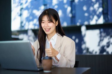 Gündelik akıllı iş kadını modern dizüstü bilgisayarla ofis binasının yanındaki masada oturuyor. Gülümseyen kadın çalışan video çağrısı yapıyor ve el sallıyor..