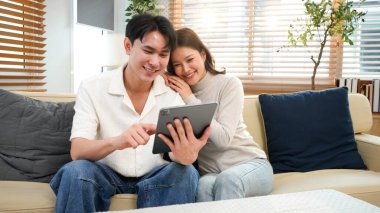 Çift evde kanepede oturup tablet oynuyor ve birlikte dinleniyorlar. Gülümsüyorlar ve mutlulukla vakit geçirmekten zevk alıyorlar...