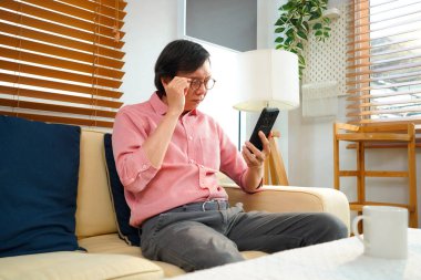 Yaşlıların sağlık sorunları konsepti, yaşlı Asyalı adamın portre fotoğrafı akıllı telefondan mesaj okumaya çalışırken uzun görüş sorunu var..