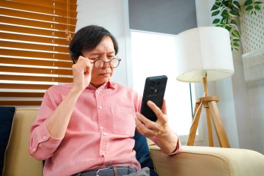Yaşlıların sağlık sorunları konsepti, yaşlı Asyalı adamın portre fotoğrafı akıllı telefondan mesaj okumaya çalışırken uzun görüş sorunu var..