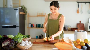 Modern mutfağın tahta tahtasında taze papaya dilimleyen bir kadın tropikal meyve hazırlama becerilerini titizlikle gösteriyor..