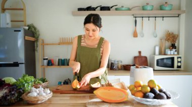 Modern mutfağın tahta tahtasında taze papaya dilimleyen bir kadın tropikal meyve hazırlama becerilerini titizlikle gösteriyor..
