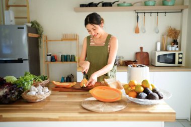 Modern mutfağın tahta tahtasında taze papaya dilimleyen bir kadın tropikal meyve hazırlama becerilerini titizlikle gösteriyor..
