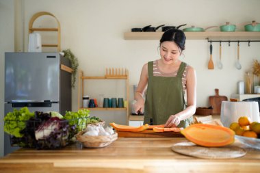 Modern mutfağın tahta tahtasında taze papaya dilimleyen bir kadın tropikal meyve hazırlama becerilerini titizlikle gösteriyor..