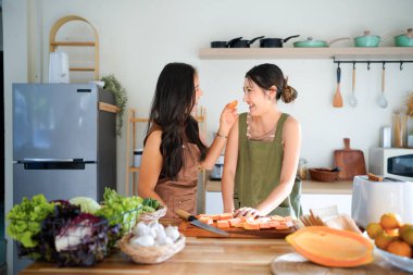 Lezbiyen bir çift, evlerindeki mutfağın sıcak atmosferinde kahvaltı hazırlıyor ve meyve paylaşıyor..